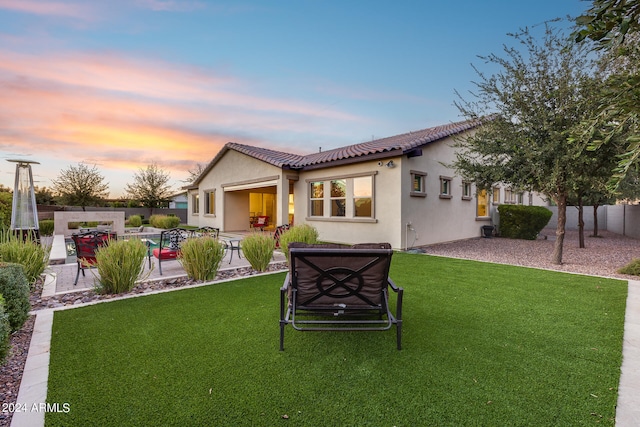 back house at dusk featuring a yard and a patio