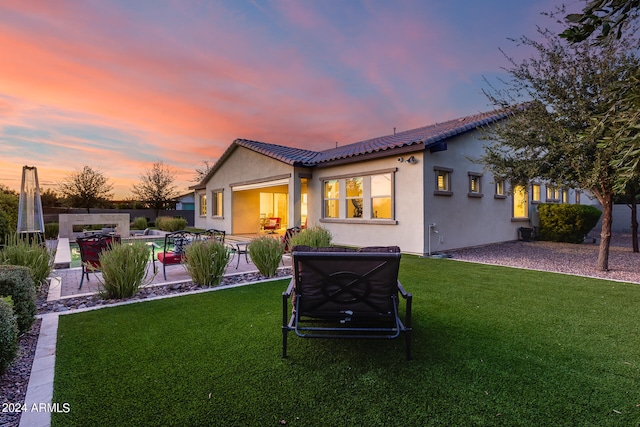 back house at dusk featuring a lawn, a swimming pool, and a patio area