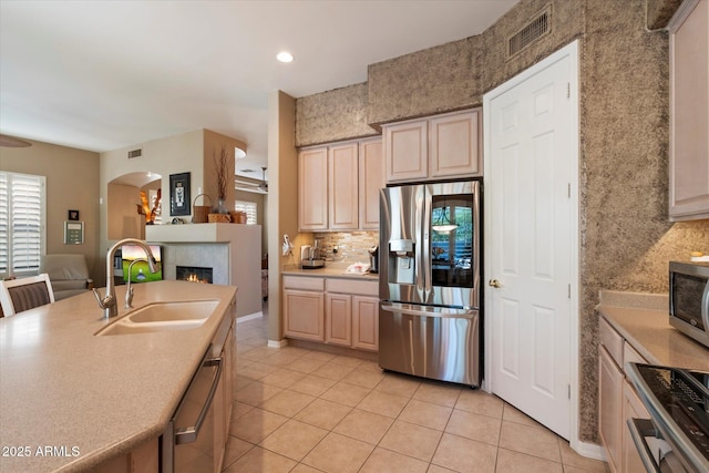 7291 E Eagle Feather Rd, Scottsdale, AZ 85266 - kitchen featuring stainless steel appliances, a sink, light tile patterned flooring, a tiled fireplace, and light countertops