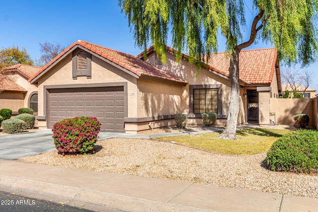 mediterranean / spanish home featuring a garage, concrete driveway, a tile roof, fence, and stucco siding