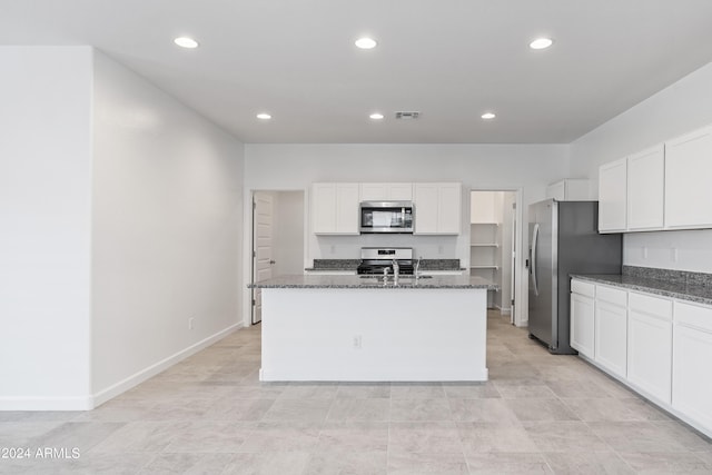 kitchen with appliances with stainless steel finishes, white cabinetry, dark stone countertops, an island with sink, and sink