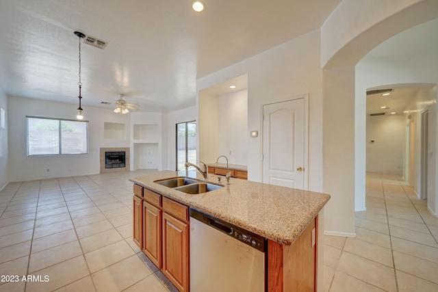 kitchen featuring built in features, an island with sink, dishwasher, sink, and a tiled fireplace