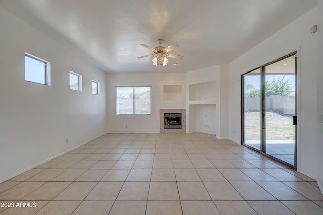 unfurnished living room featuring ceiling fan, a fireplace, light tile flooring, and a healthy amount of sunlight