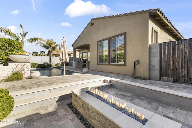 rear view of property featuring a patio, a fire pit, fence, and stucco siding