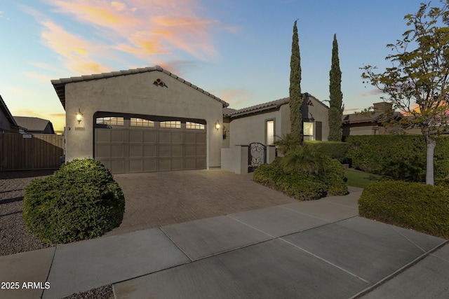 mediterranean / spanish-style house featuring a gate, stucco siding, a garage, a tile roof, and decorative driveway