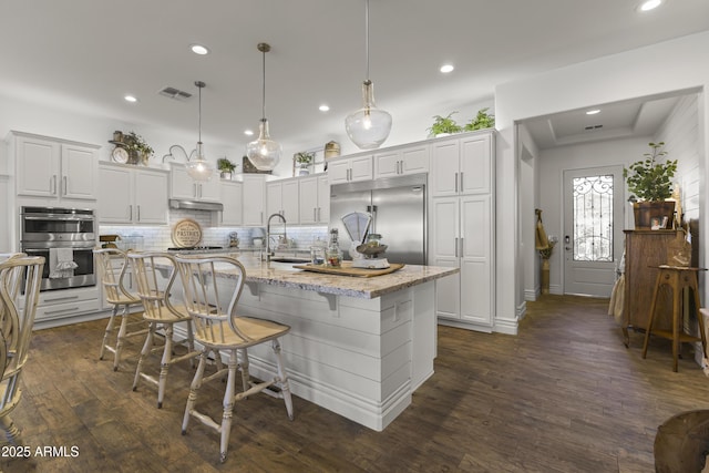 kitchen with visible vents, backsplash, dark wood-type flooring, appliances with stainless steel finishes, and a sink