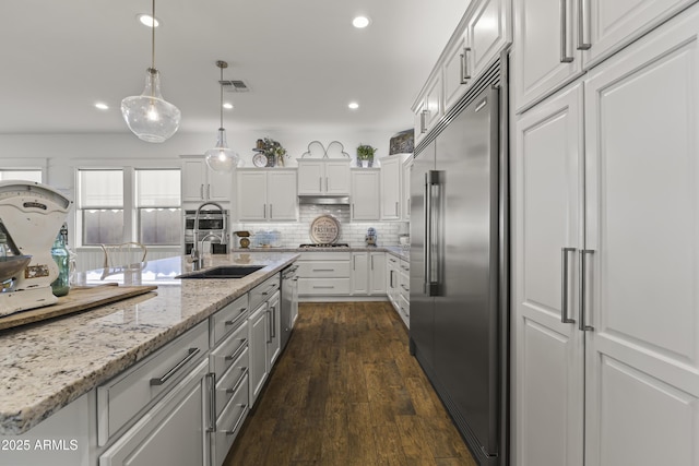 kitchen with dark wood-type flooring, decorative backsplash, appliances with stainless steel finishes, white cabinetry, and a sink