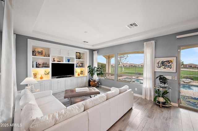 living room with a tray ceiling, built in features, and light wood-type flooring