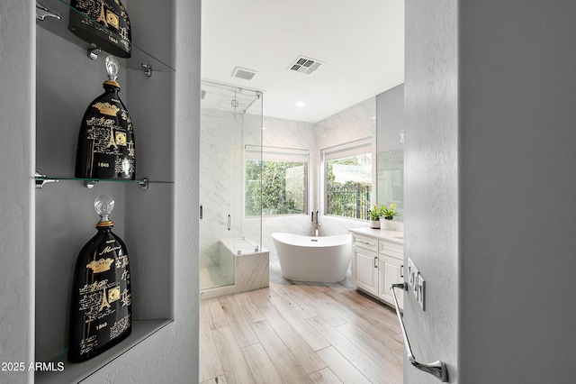 full bath with visible vents, wood finished floors, a stall shower, a freestanding tub, and vanity