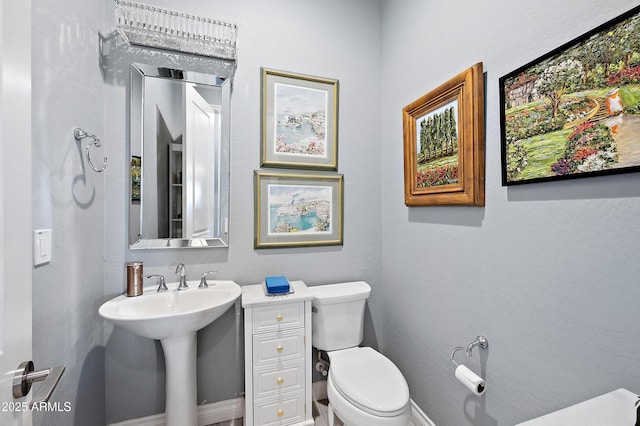 bathroom featuring toilet, baseboards, and a sink