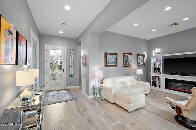 foyer entrance with visible vents, light wood finished floors, baseboards, recessed lighting, and a glass covered fireplace