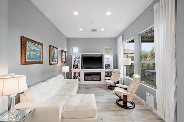 living area featuring visible vents, baseboards, light wood-type flooring, recessed lighting, and a glass covered fireplace