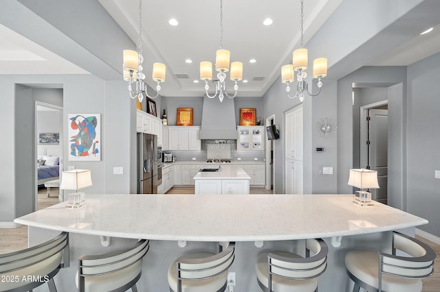 kitchen featuring hanging light fixtures, tasteful backsplash, premium range hood, a spacious island, and white cabinets