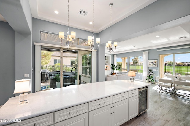 kitchen with white cabinetry, beverage cooler, an inviting chandelier, a raised ceiling, and decorative light fixtures