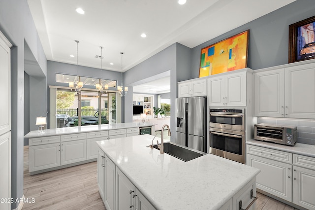 kitchen with a sink, a chandelier, a toaster, stainless steel appliances, and a kitchen island with sink