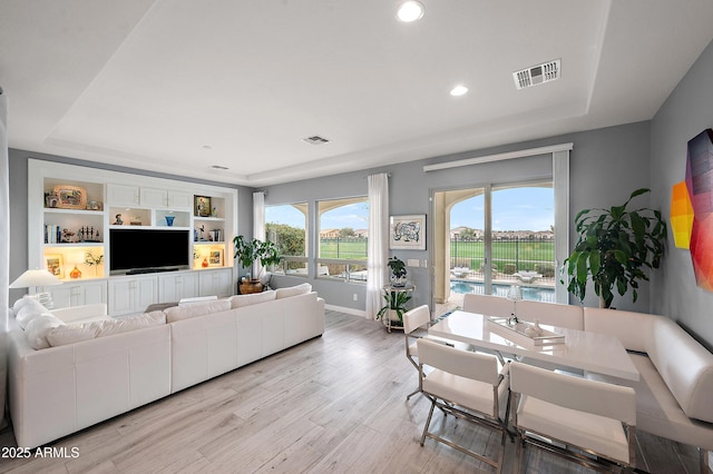 living area featuring visible vents, light wood-style flooring, and a raised ceiling