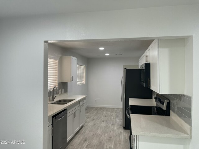 kitchen with white cabinetry, sink, backsplash, appliances with stainless steel finishes, and light wood-type flooring