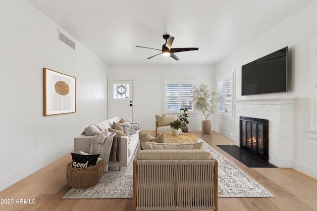 living room featuring ceiling fan, light hardwood / wood-style floors, and a fireplace