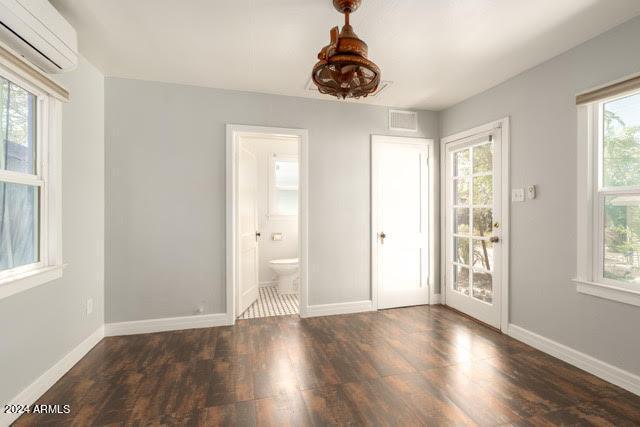 unfurnished bedroom featuring ensuite bath, dark wood-type flooring, an AC wall unit, and access to outside