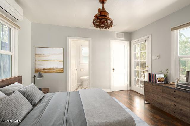 bedroom featuring dark wood-type flooring, connected bathroom, and a wall unit AC