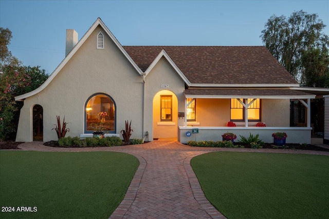 view of front of house with stucco siding, a chimney, a porch, and a front lawn