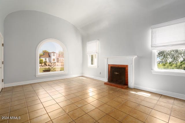 unfurnished living room featuring lofted ceiling, a brick fireplace, and light tile patterned flooring