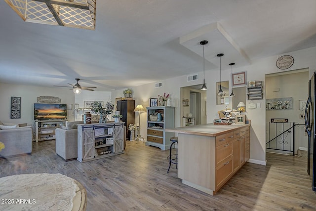 kitchen featuring wood finished floors, open floor plan, light brown cabinetry, a breakfast bar area, and ceiling fan
