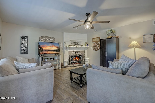 living room featuring wood finished floors, a stone fireplace, and ceiling fan