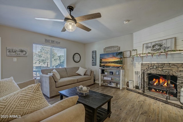 living area with a stone fireplace, wood finished floors, and ceiling fan
