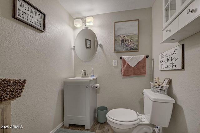 bathroom with baseboards, wood finished floors, toilet, and vanity