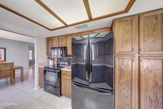 kitchen with brown cabinets, light countertops, light tile patterned floors, visible vents, and black appliances