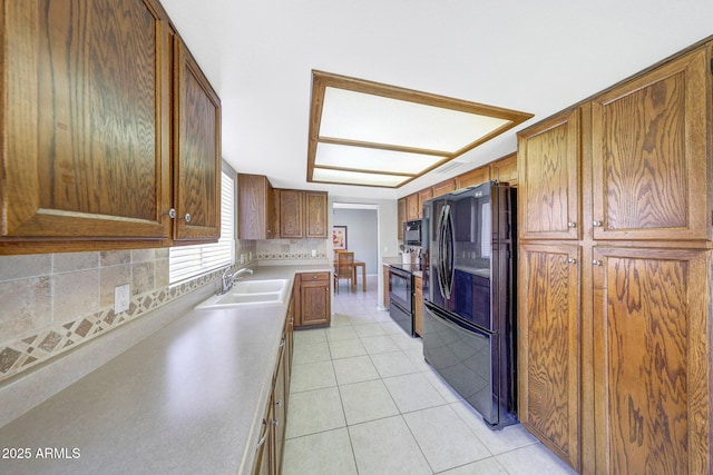 kitchen featuring a sink, brown cabinetry, light tile patterned floors, tasteful backsplash, and black appliances