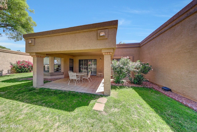 rear view of property with a lawn, a patio, and stucco siding