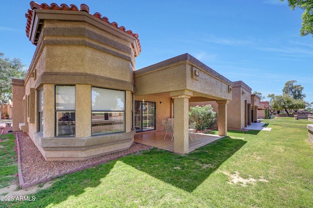 back of house featuring a lawn, a patio area, stucco siding, and a tile roof