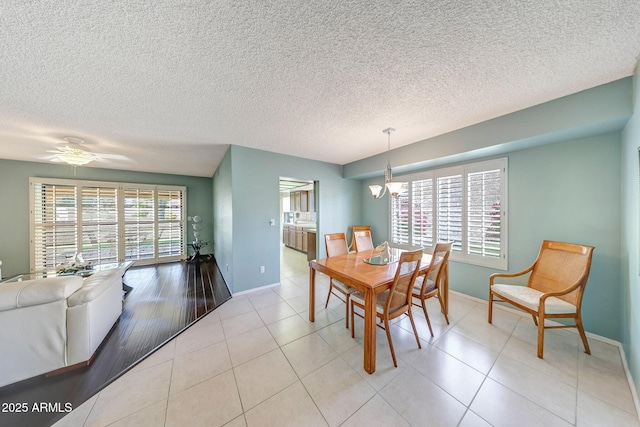 dining area featuring light tile patterned floors, baseboards, ceiling fan with notable chandelier, and a textured ceiling