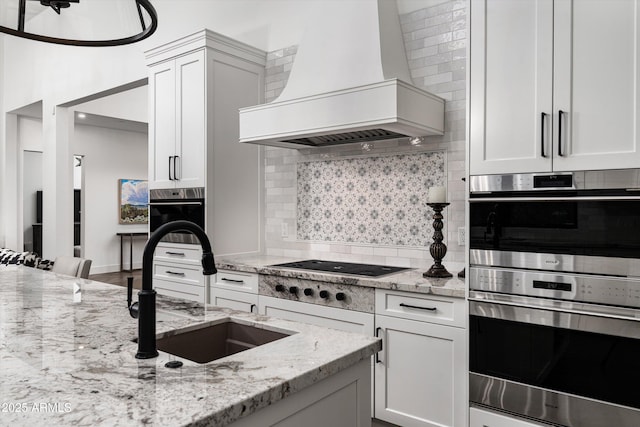kitchen with tasteful backsplash, a sink, premium range hood, white cabinets, and double oven