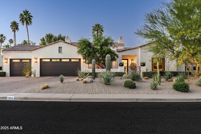 mediterranean / spanish-style home with decorative driveway, a garage, stucco siding, and a tile roof