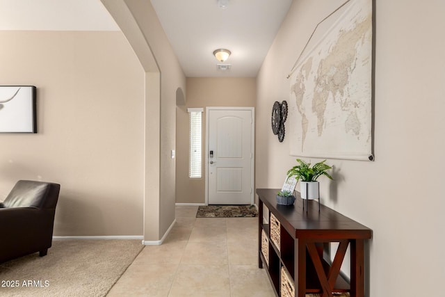 entryway with arched walkways, light tile patterned floors, visible vents, and baseboards