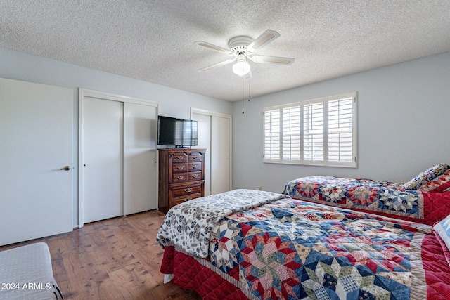 bedroom featuring a textured ceiling, ceiling fan, wood finished floors, and multiple closets