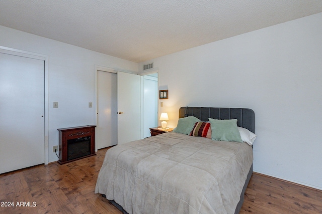 bedroom with multiple closets, visible vents, a textured ceiling, and wood finished floors