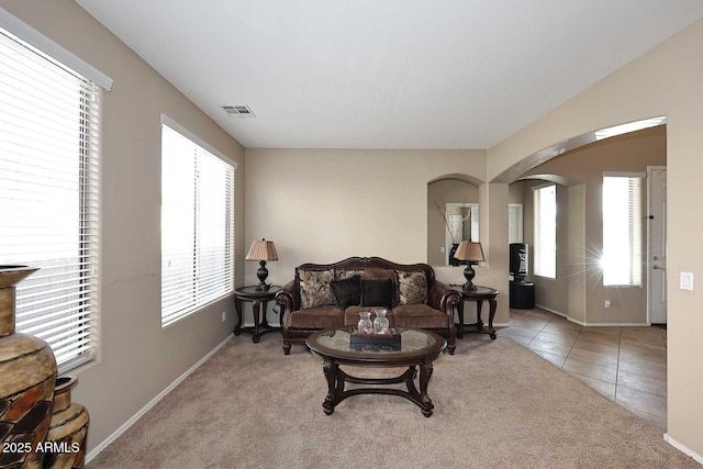 tiled living area with arched walkways, carpet flooring, visible vents, and a healthy amount of sunlight