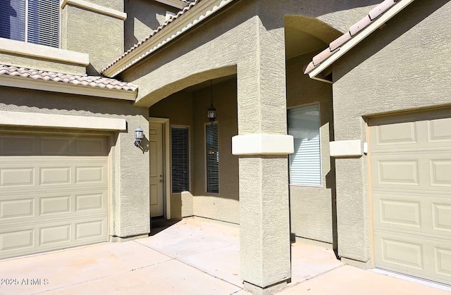 view of exterior entry with a garage, a tiled roof, and stucco siding