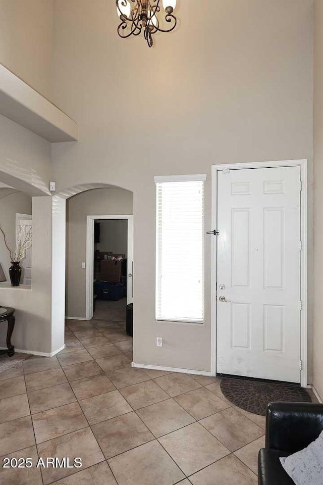 entrance foyer with arched walkways, light tile patterned floors, a high ceiling, and an inviting chandelier