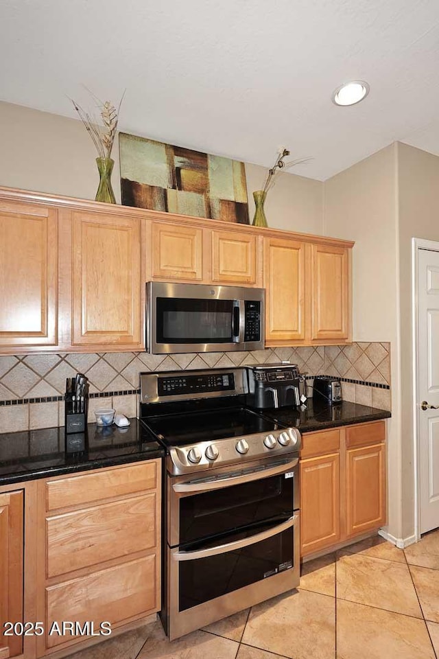 kitchen with light tile patterned floors, decorative backsplash, light brown cabinetry, appliances with stainless steel finishes, and dark stone counters