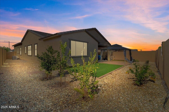 19447 W Mariposa Dr, Litchfield Park, AZ 85340 - back of property at dusk featuring a gazebo, cooling unit, a patio area, stucco siding, and a fenced backyard