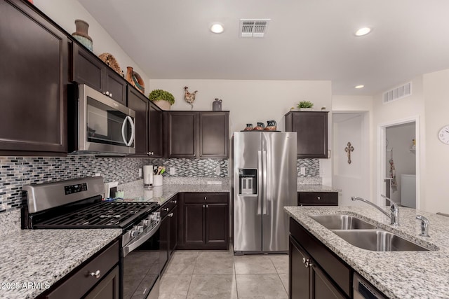 kitchen with dark brown cabinetry, sink, light stone counters, stainless steel appliances, and decorative backsplash