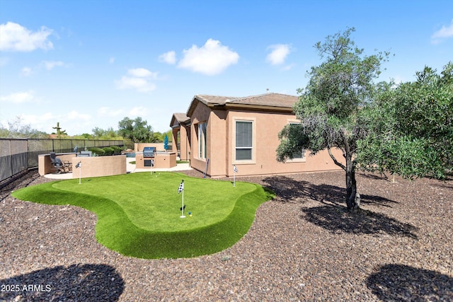 13072 W Alyssa Ln, Peoria, AZ 85383 - back of house featuring an area to practice putting, a fenced backyard, stucco siding, a patio area, and exterior kitchen