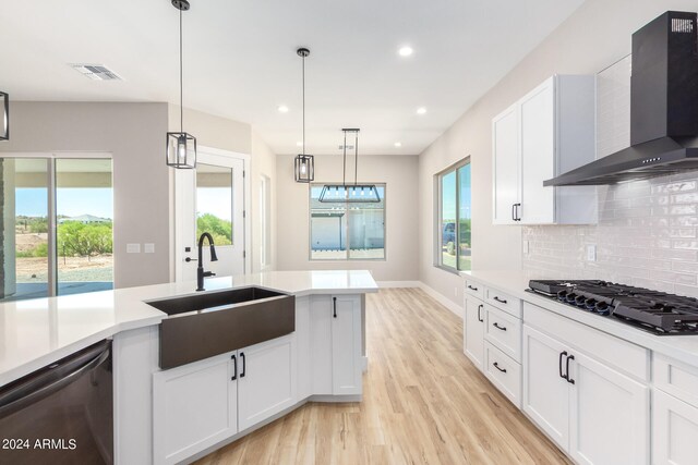 kitchen with hanging light fixtures, light hardwood / wood-style floors, wall chimney exhaust hood, dishwasher, and gas cooktop