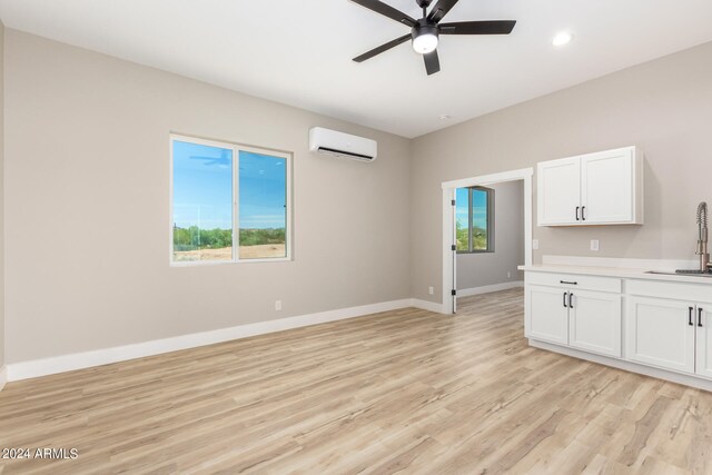 unfurnished living room with ceiling fan, a wall mounted AC, sink, and light hardwood / wood-style flooring