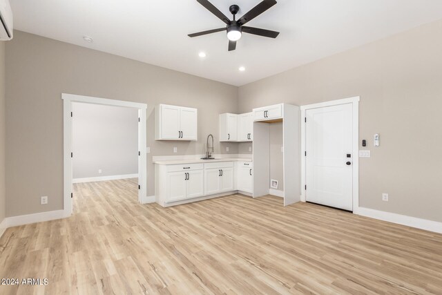 interior space with white cabinets, light wood-type flooring, ceiling fan, a wall unit AC, and sink